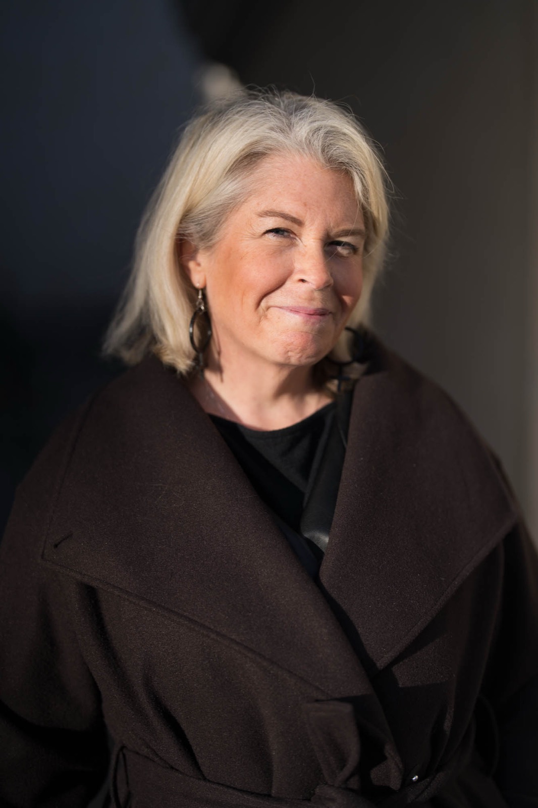 Portrait of Carina in a brown coat, sunlight against a dark background