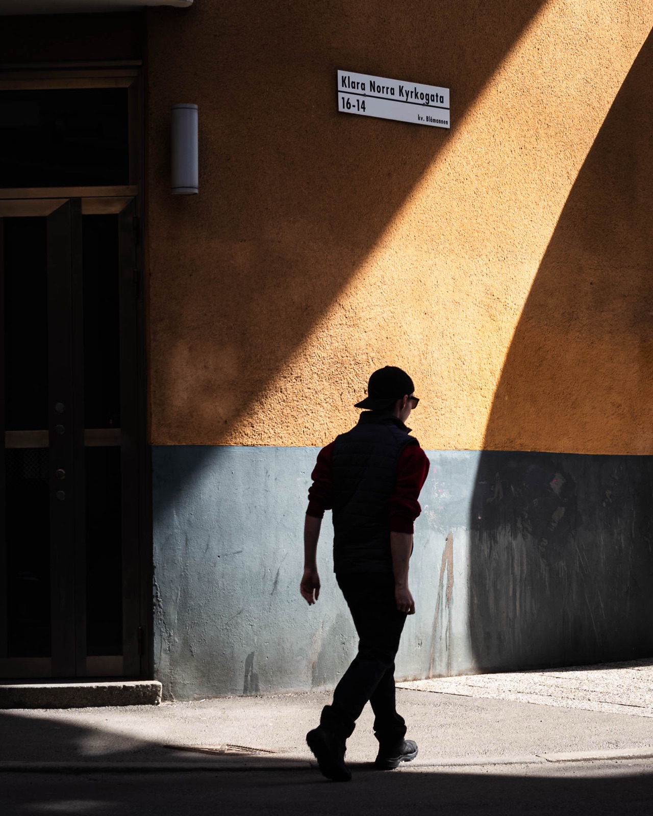 Man in a cap passing a sunlit ochre wall